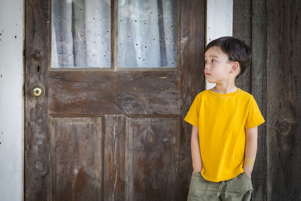 Melancholy Mixed Race Boy Standing In Front of Door